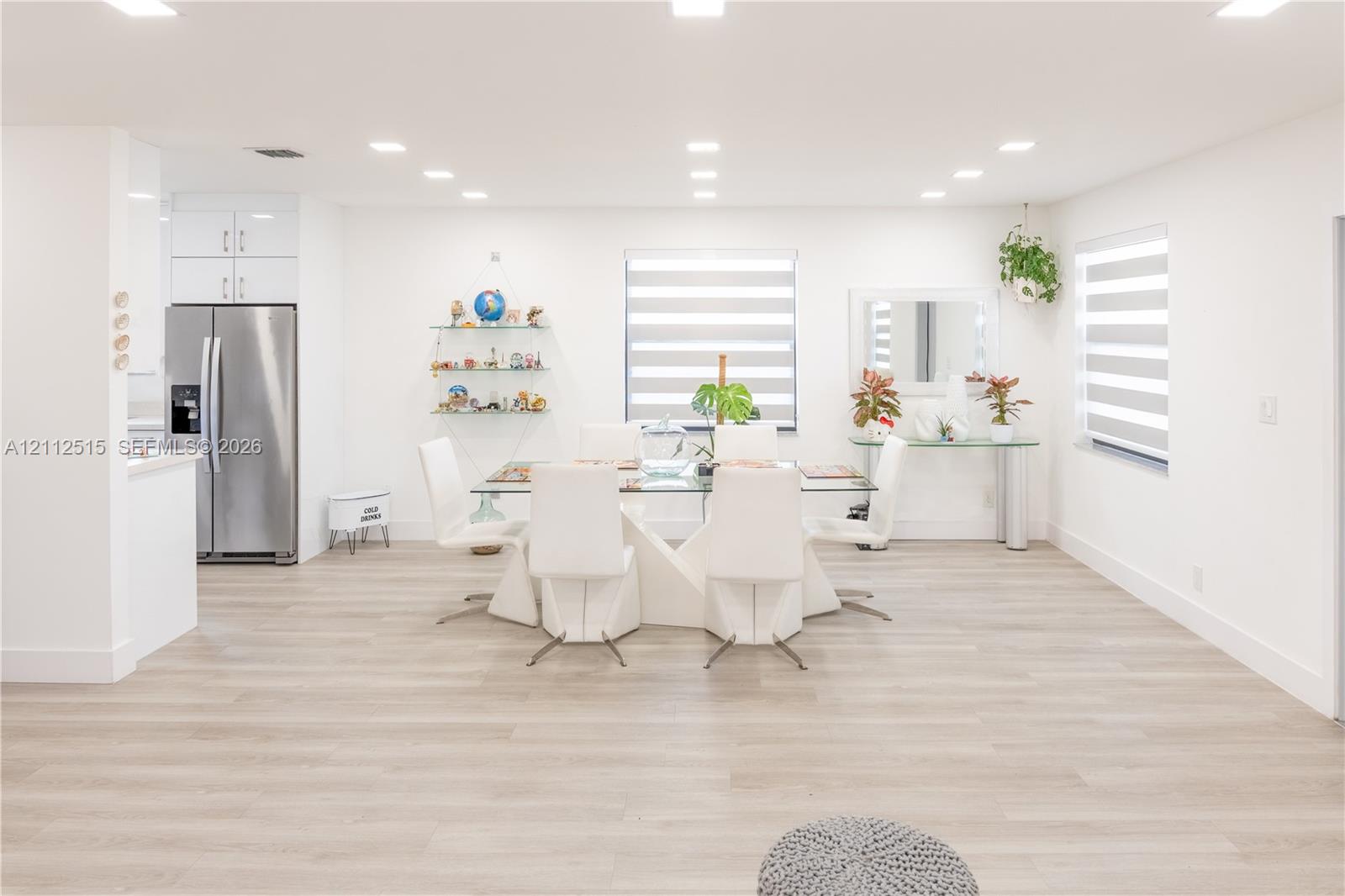Open-concept interior featuring light wood-finish flooring, recessed lighting, white gloss cabinetry, and dual-layered window treatments