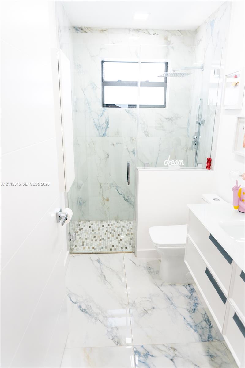 Bathroom featuring large-format veined tile flooring, a glass-enclosed shower with mosaic tile floor, a wall-mounted floating vanity, and a minimalist toilet