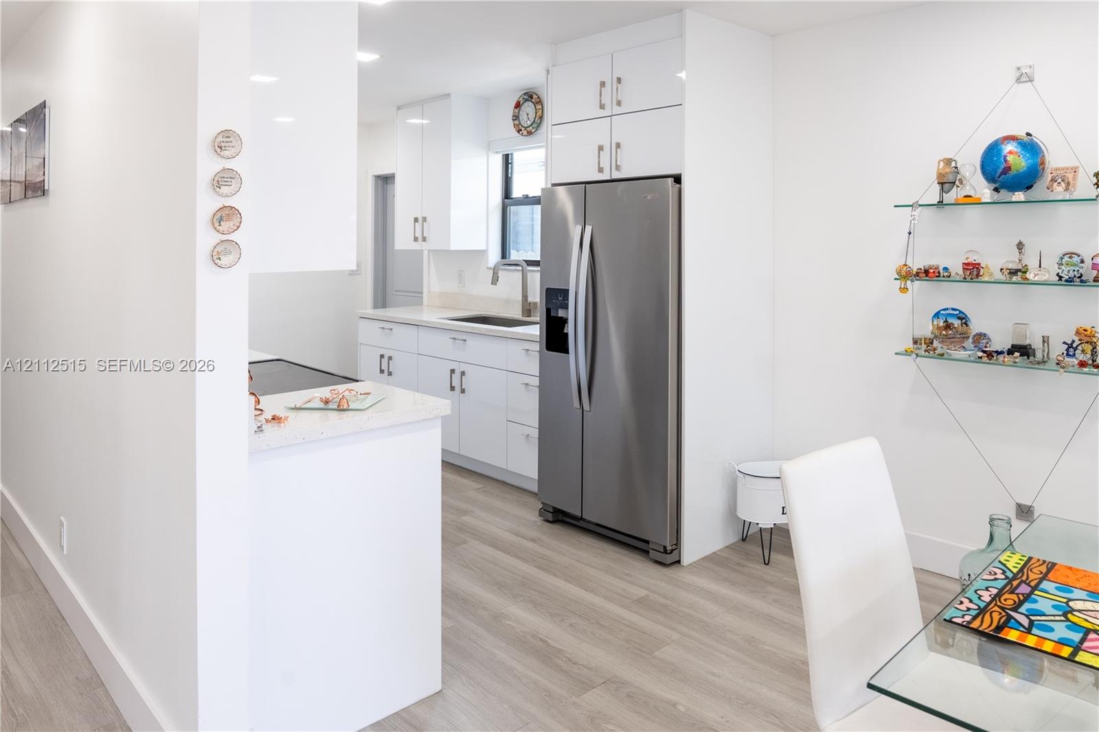 Kitchen featuring high-gloss white cabinetry, stainless steel side-by-side refrigerator, light-toned stone-finish countertops, and wood-finish flooring