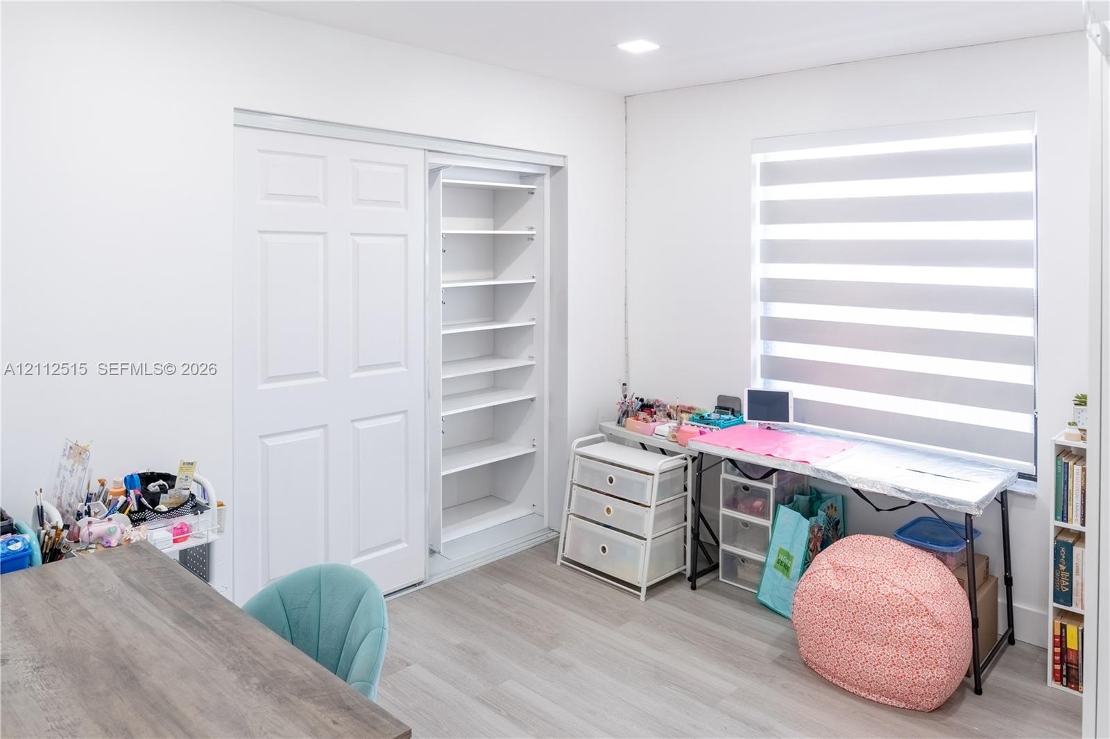 Room featuring light-toned wood-finish flooring, recessed ceiling lighting, a built-in closet with multi-tier shelving, and dual-layered cellular shades