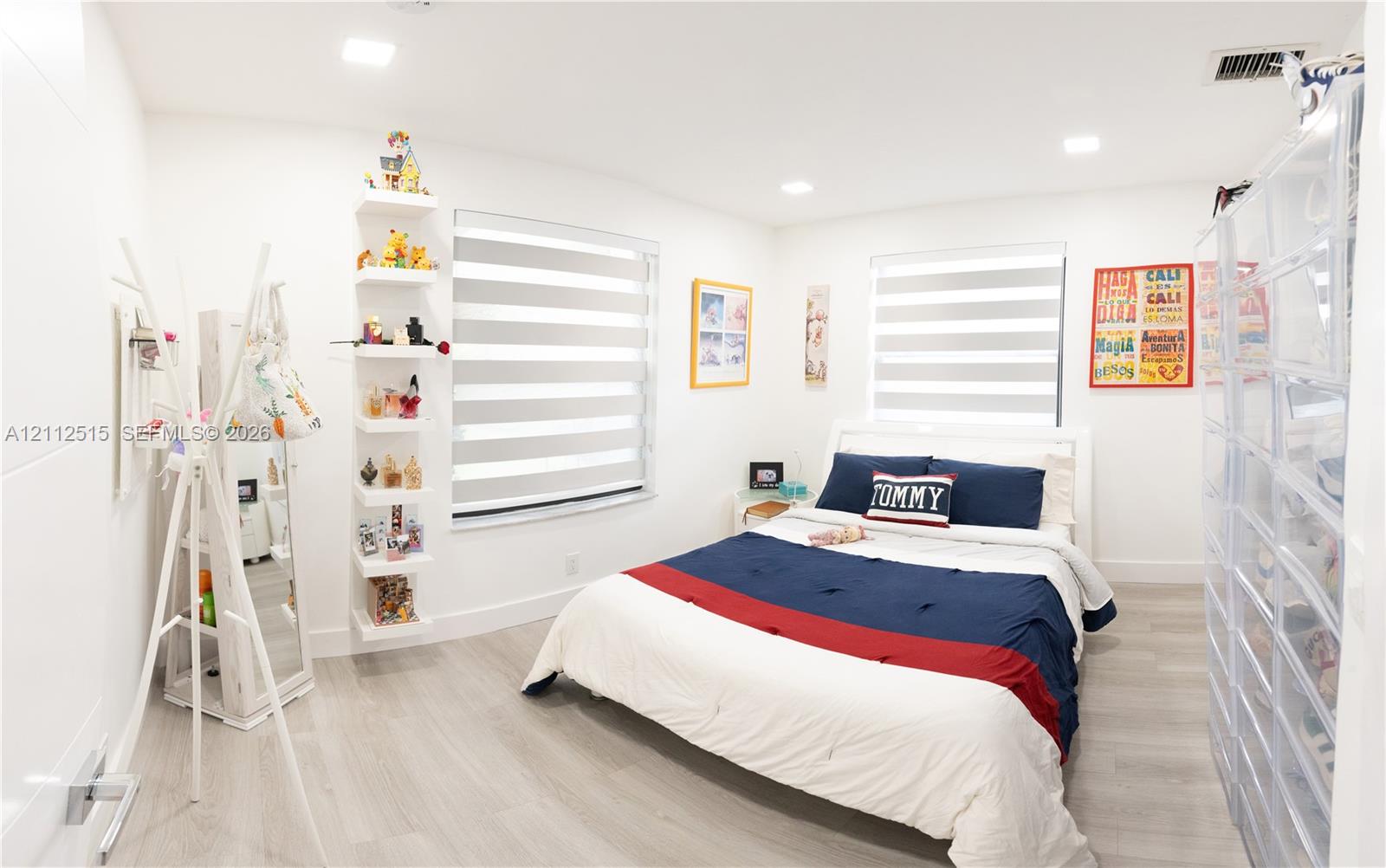 Interior room featuring wood-finish flooring, recessed lighting, dual windows with fitted light-filtering shades, and custom built-in wall shelving