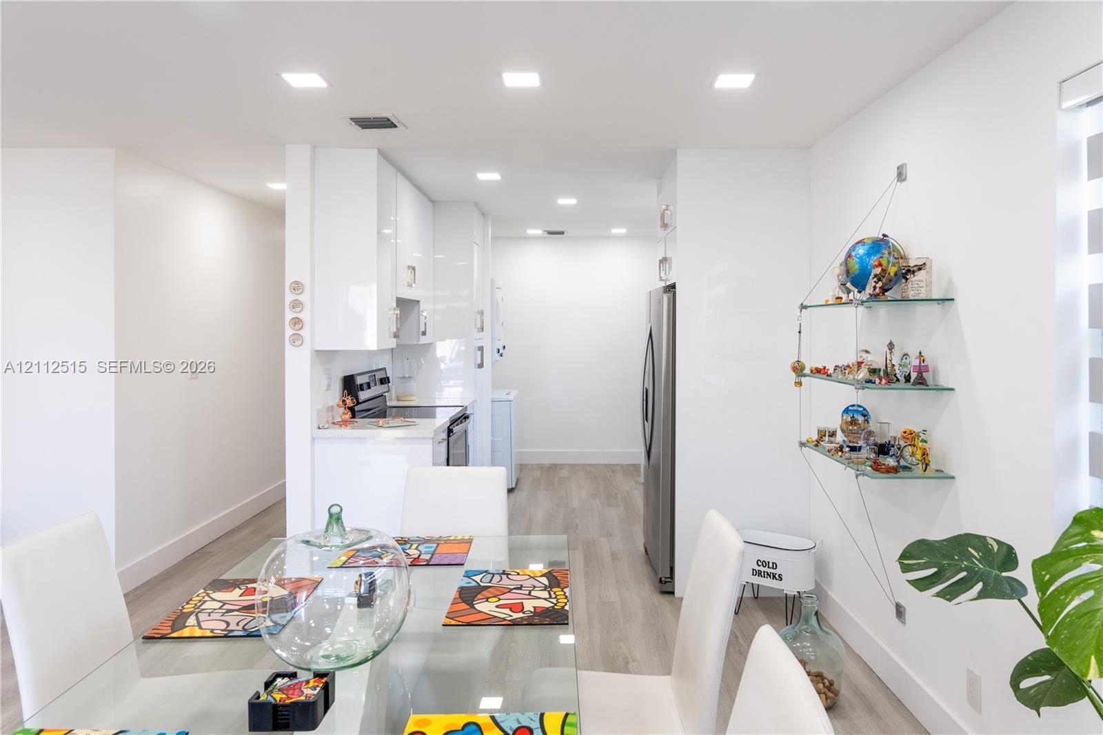Glossy white flat-panel cabinetry, stainless steel appliances, wood-finish flooring, and recessed ceiling lighting