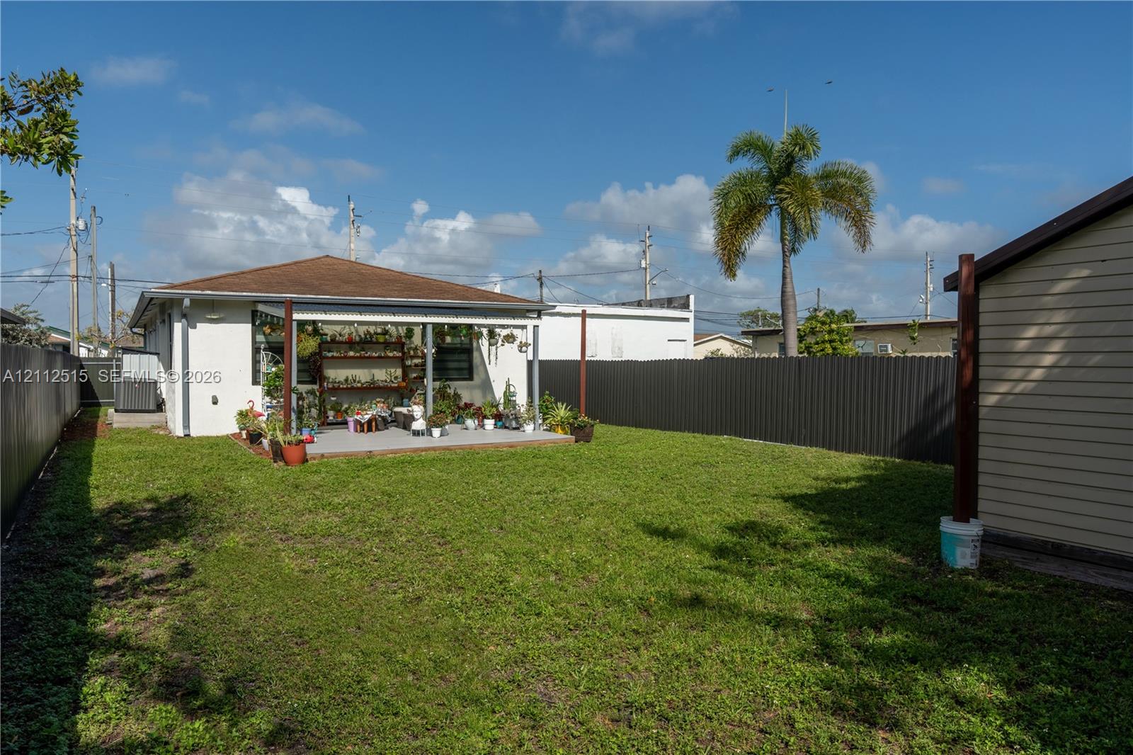 Rear exterior featuring a concrete patio, a covered pergola, and a private metal perimeter fence surrounding the lawn