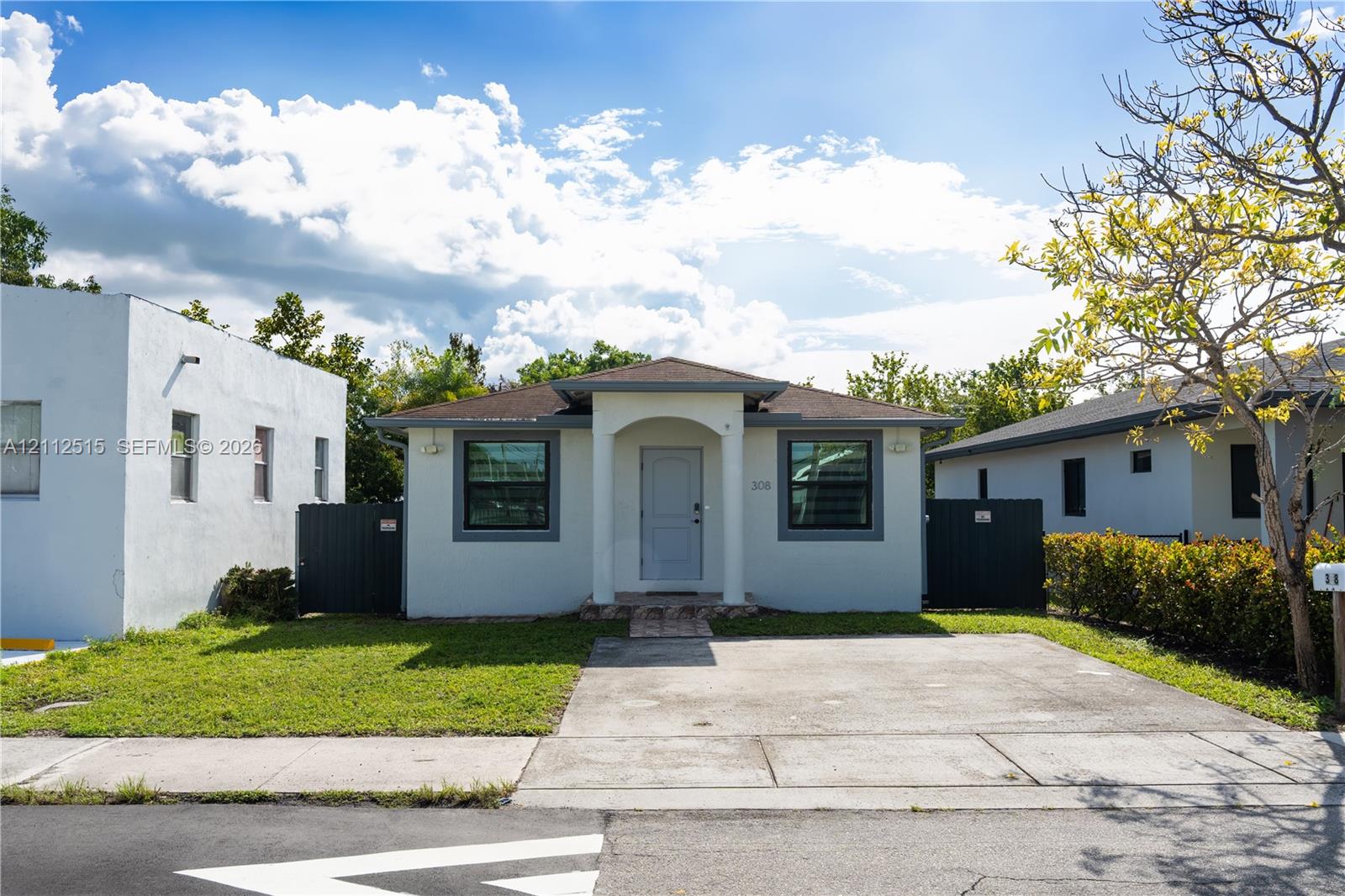 Single-story exterior featuring a stucco facade, covered front entryway with architectural pillars, concrete driveway, and gated side access