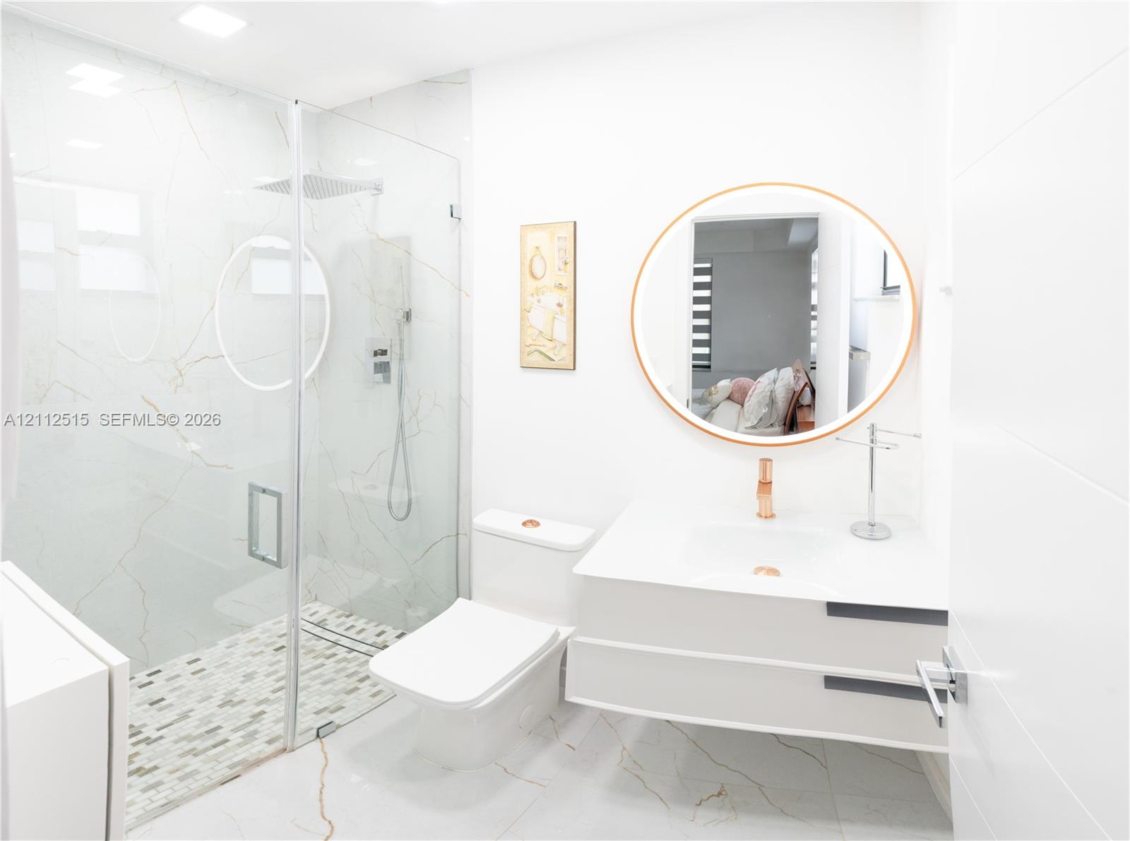 Floating vanity with a smooth white countertop, large-format stone-patterned wall tiles, glass-enclosed walk-in shower, pebble-mosaic shower flooring, and a circular wall-mounted mirror