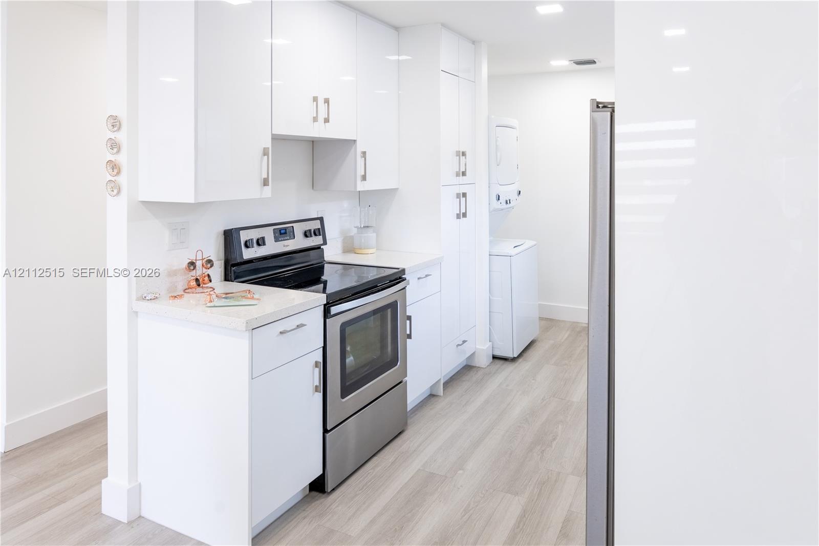 Kitchen featuring white slab-front cabinetry, stainless steel range, light-toned stone-finish countertops, wood-finish flooring, and recessed ceiling lighting
