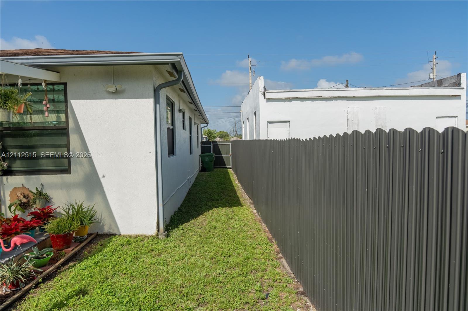 Exterior side yard featuring a stucco-finished wall, corrugated metal privacy fencing, and a sodded lawn area