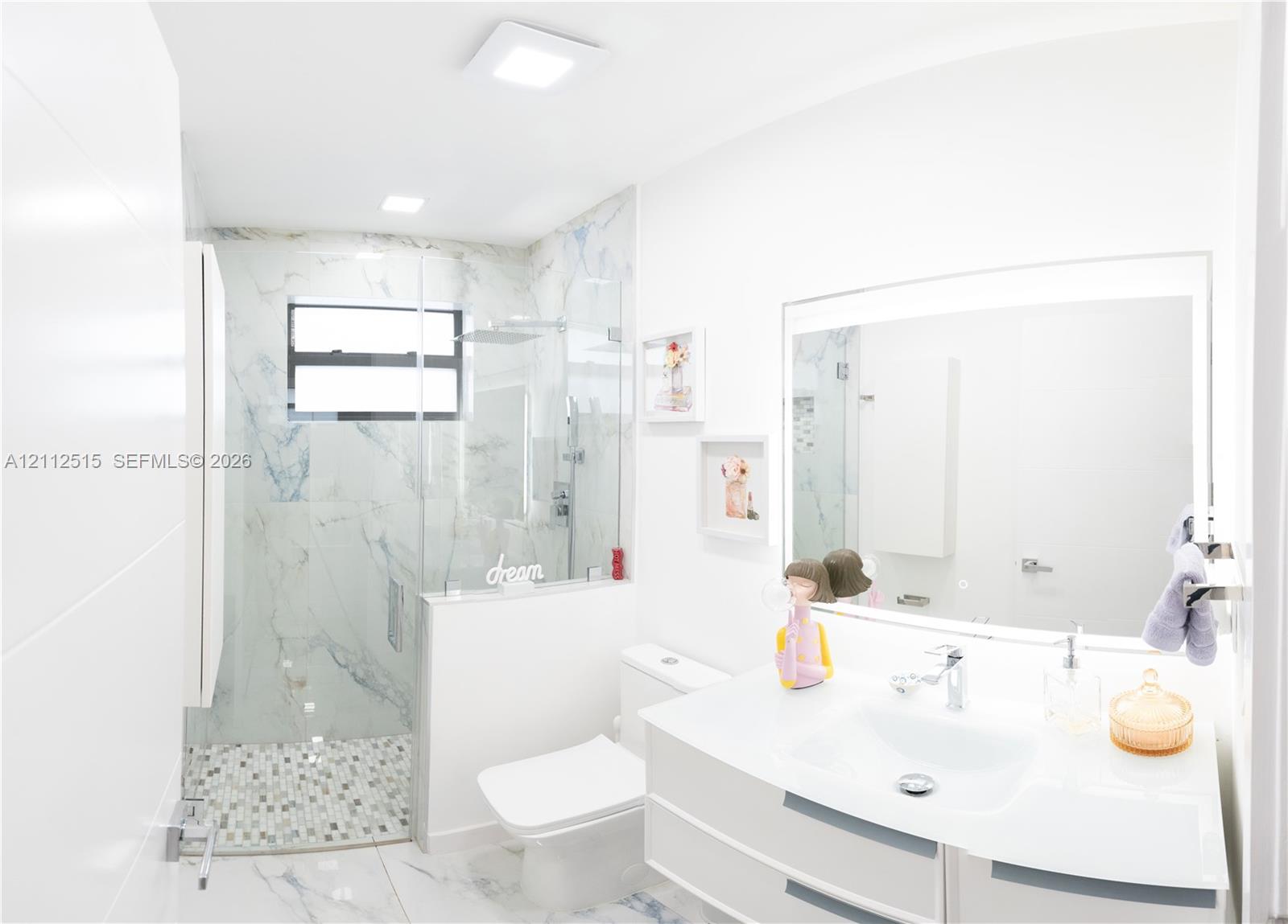 Floating vanity with integrated sink, walk-in shower featuring glass enclosure, stone-finish wall tiling, mosaic tile shower floor, and large-format floor tile