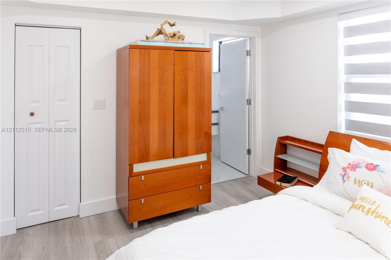 Room featuring wood-finish flooring, a white bifold closet door, and a horizontal-slat window shade