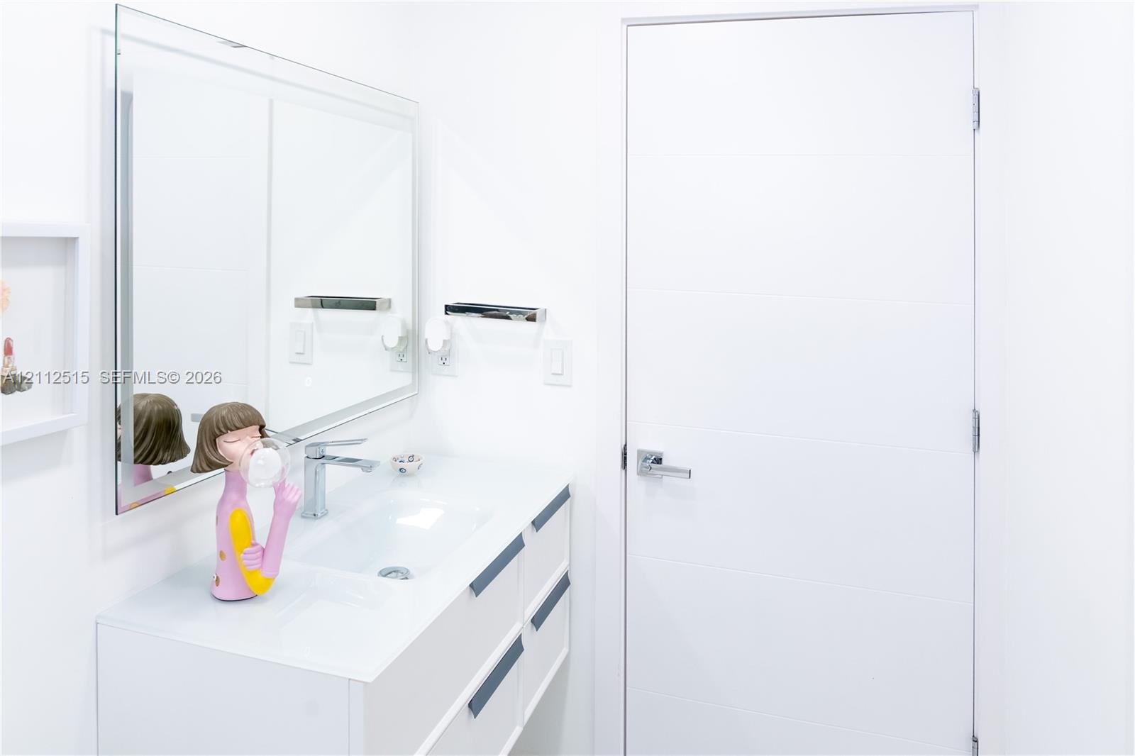 Wall-mounted mirror, white floating vanity with integrated sink, chrome faucet, and flat-panel door with metallic lever hardware