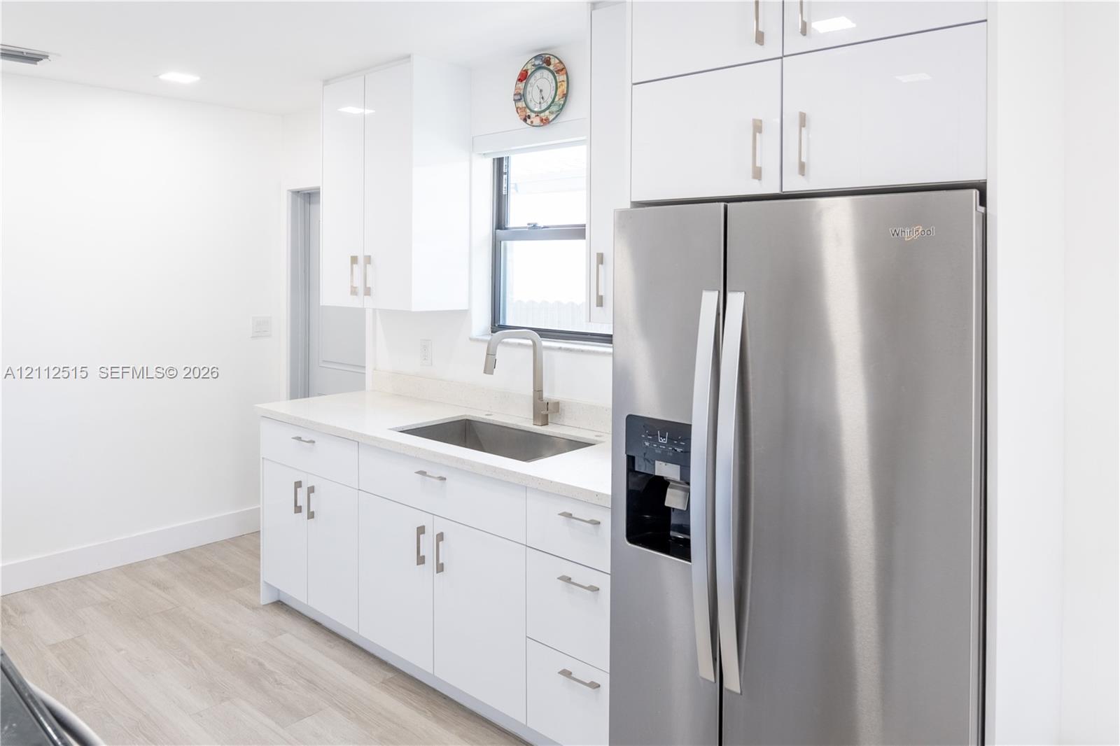 Kitchen featuring high-gloss white cabinetry, solid-surface countertops, stainless steel side-by-side refrigerator, under-mount sink with gooseneck faucet, and wood-finish flooring