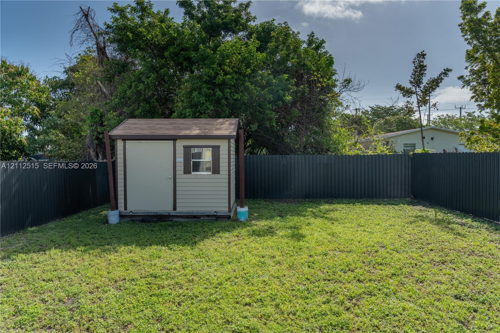 Backyard area featuring a storage shed, grass lawn, and dark metal privacy fencing