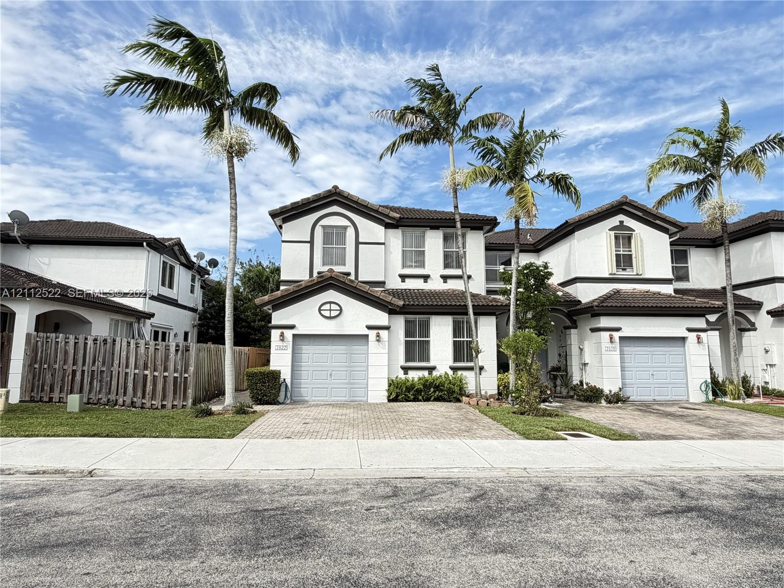 Two-story multi-unit exterior featuring a stucco facade, decorative arched window accents, attached garages, and paver driveways