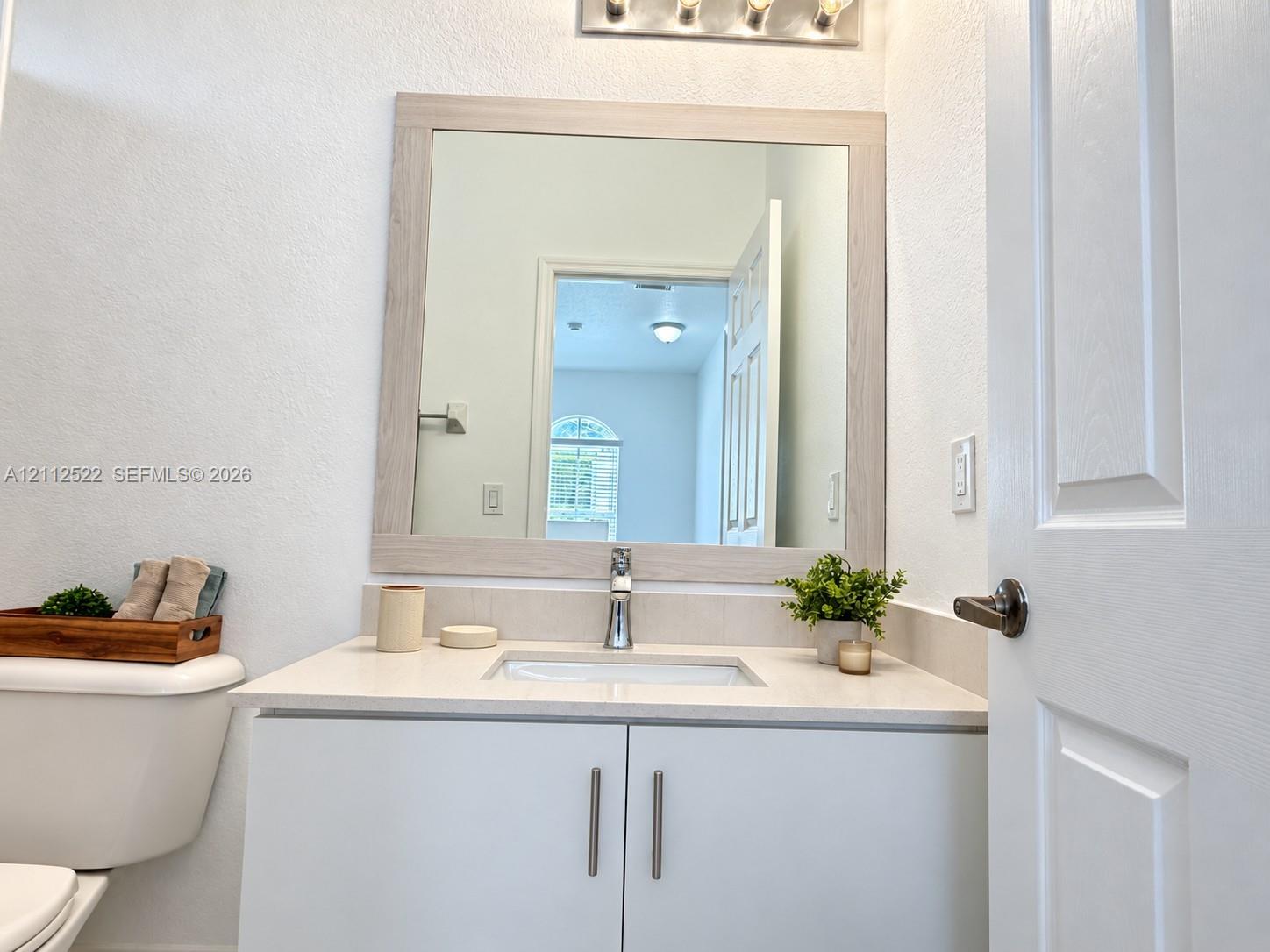 Vanity featuring a light-toned wood-finish frame mirror, stone-composite countertop, undermount sink, and minimalist hardware