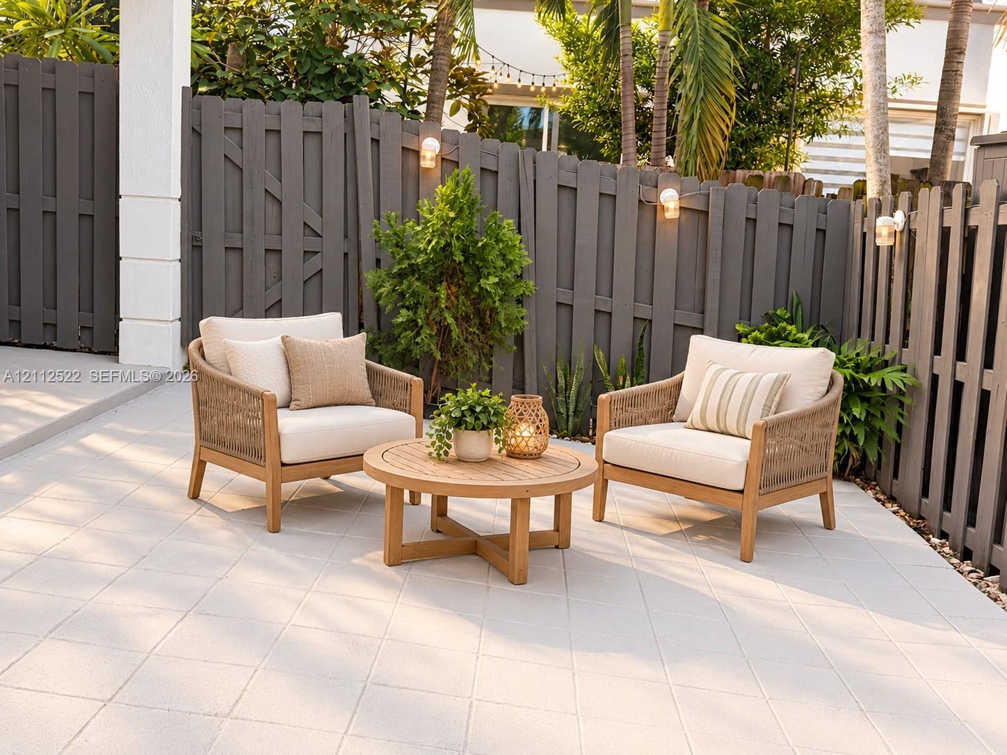 Tiled patio featuring a privacy fence, mature landscaping, and wall-mounted exterior lighting
