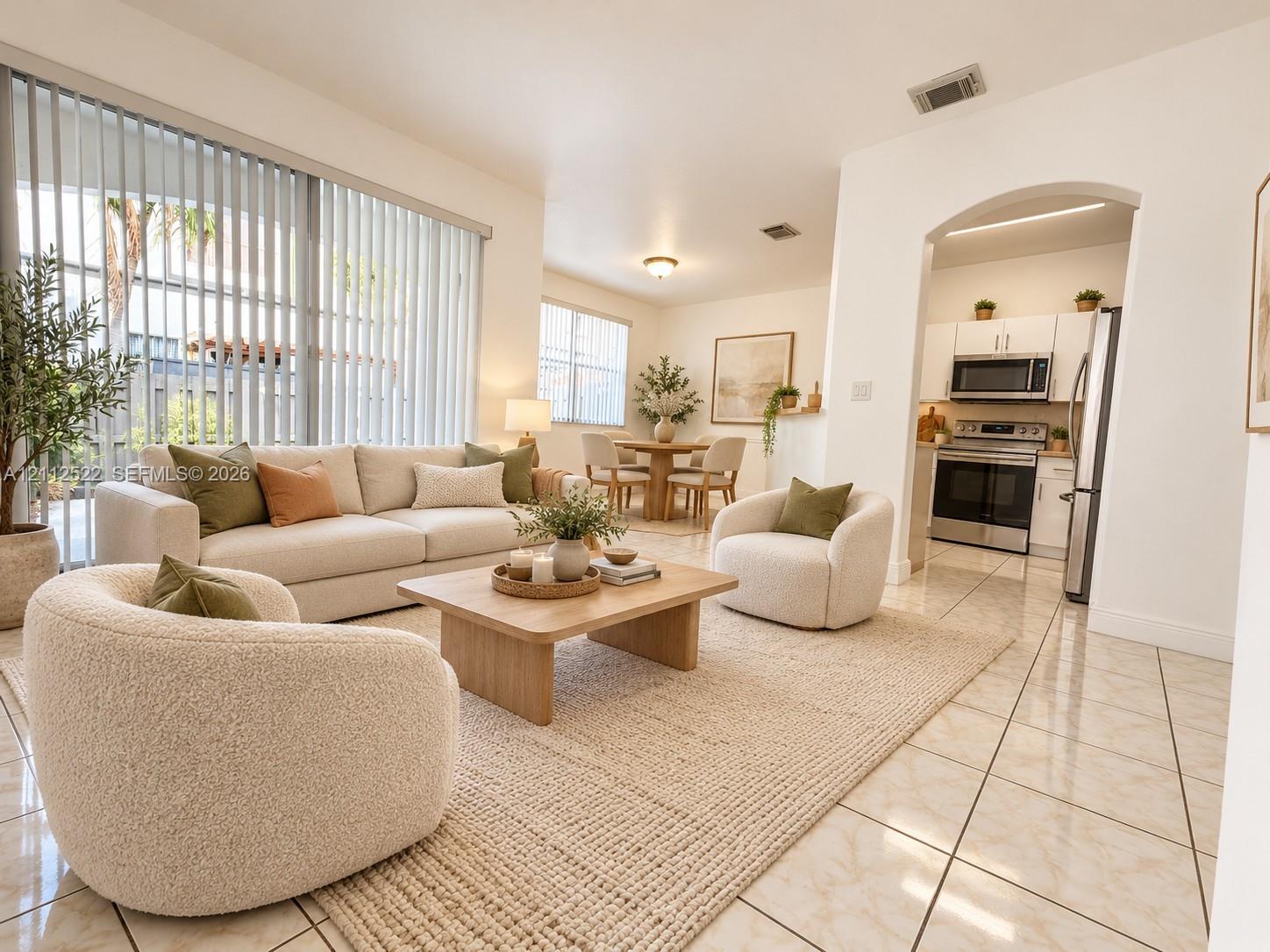 Open-concept living space with polished tile flooring, floor-to-ceiling vertical blinds, recessed lighting, and a kitchen featuring an arched entryway and stainless steel appliances