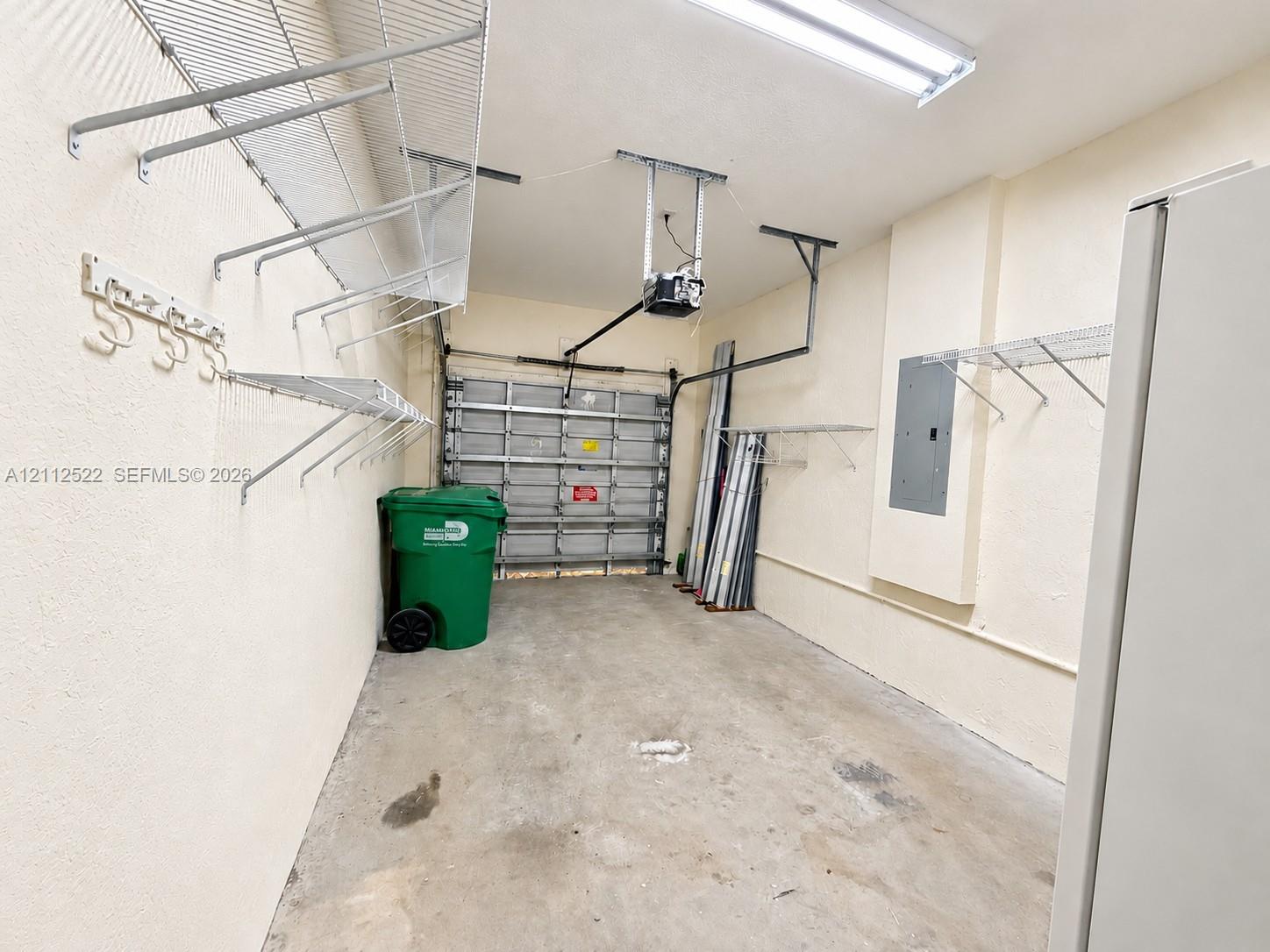 Garage interior featuring concrete flooring, a metal roll-up door, overhead fluorescent lighting, and extensive wall-mounted wire shelving