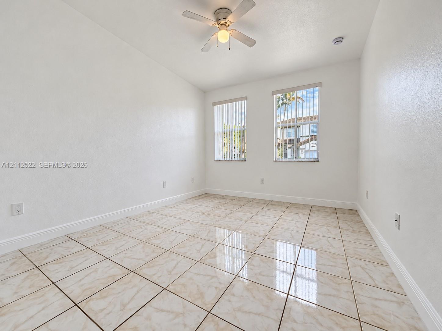 Interior room featuring large-format ceramic tile flooring, dual windows with vertical blinds, and a central ceiling fan