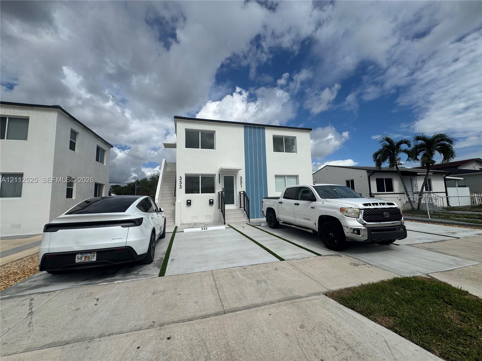 Two-story exterior featuring white stucco finish, blue vertical siding accents, concrete driveway with green space strips, and exterior staircase