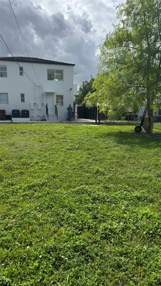 Expansive backyard featuring a large grass lawn, mature trees, and a concrete patio area