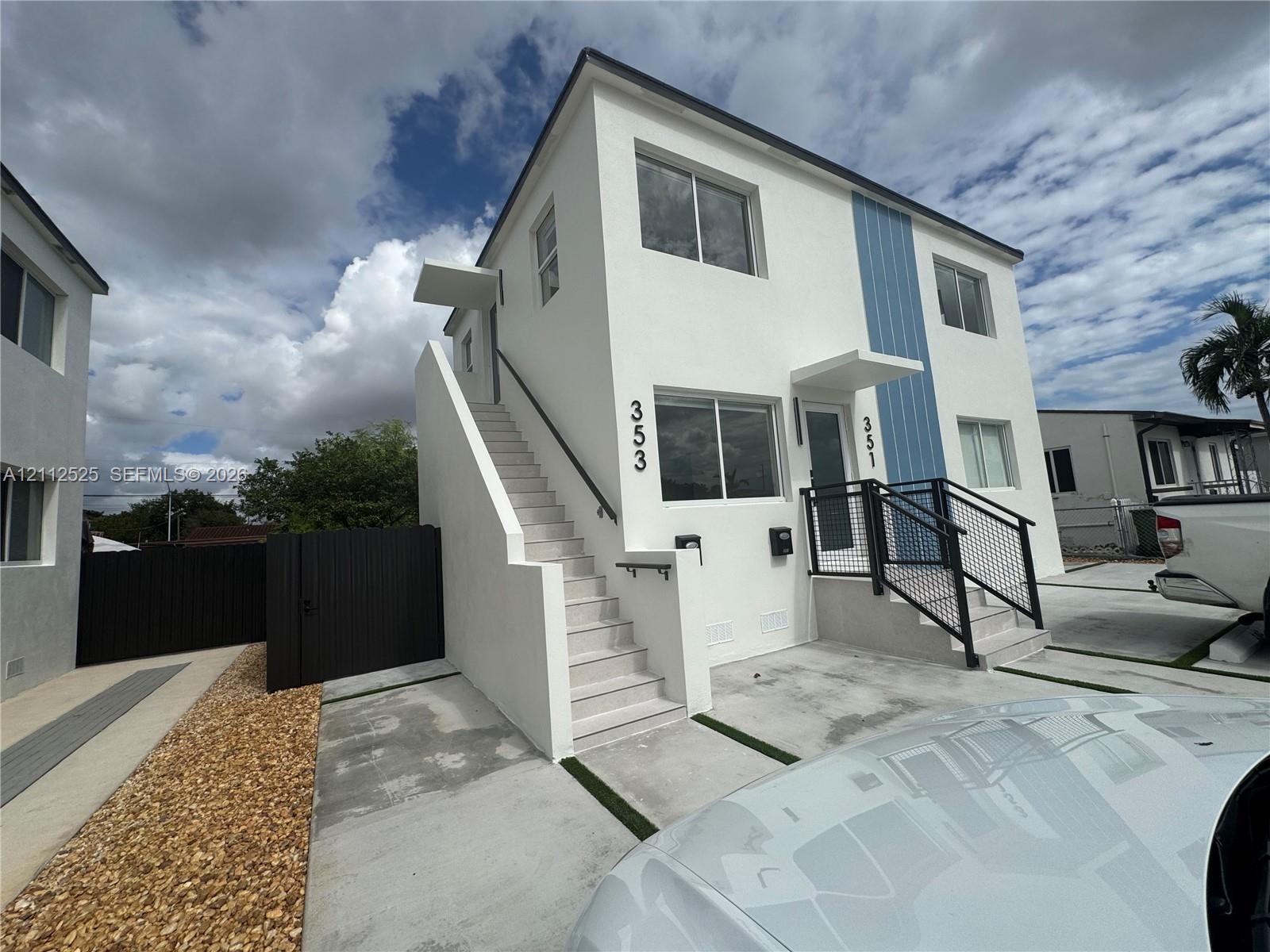 Two-story exterior featuring white stucco finish, blue vertical siding accents, concrete staircases with metal handrails, and a dedicated concrete parking area