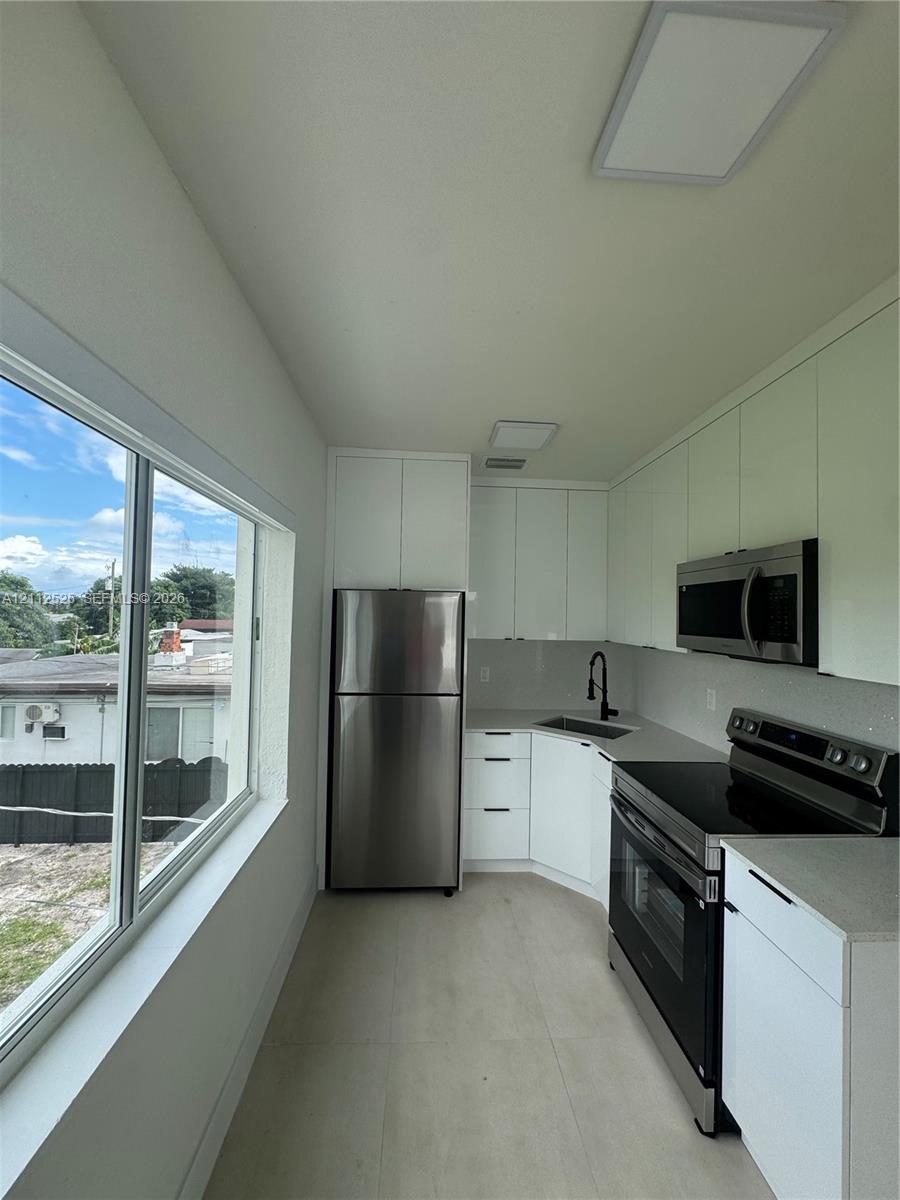 Kitchen featuring white high-gloss cabinetry, stainless steel appliances, solid-surface countertops, a matte black faucet, and expansive windows