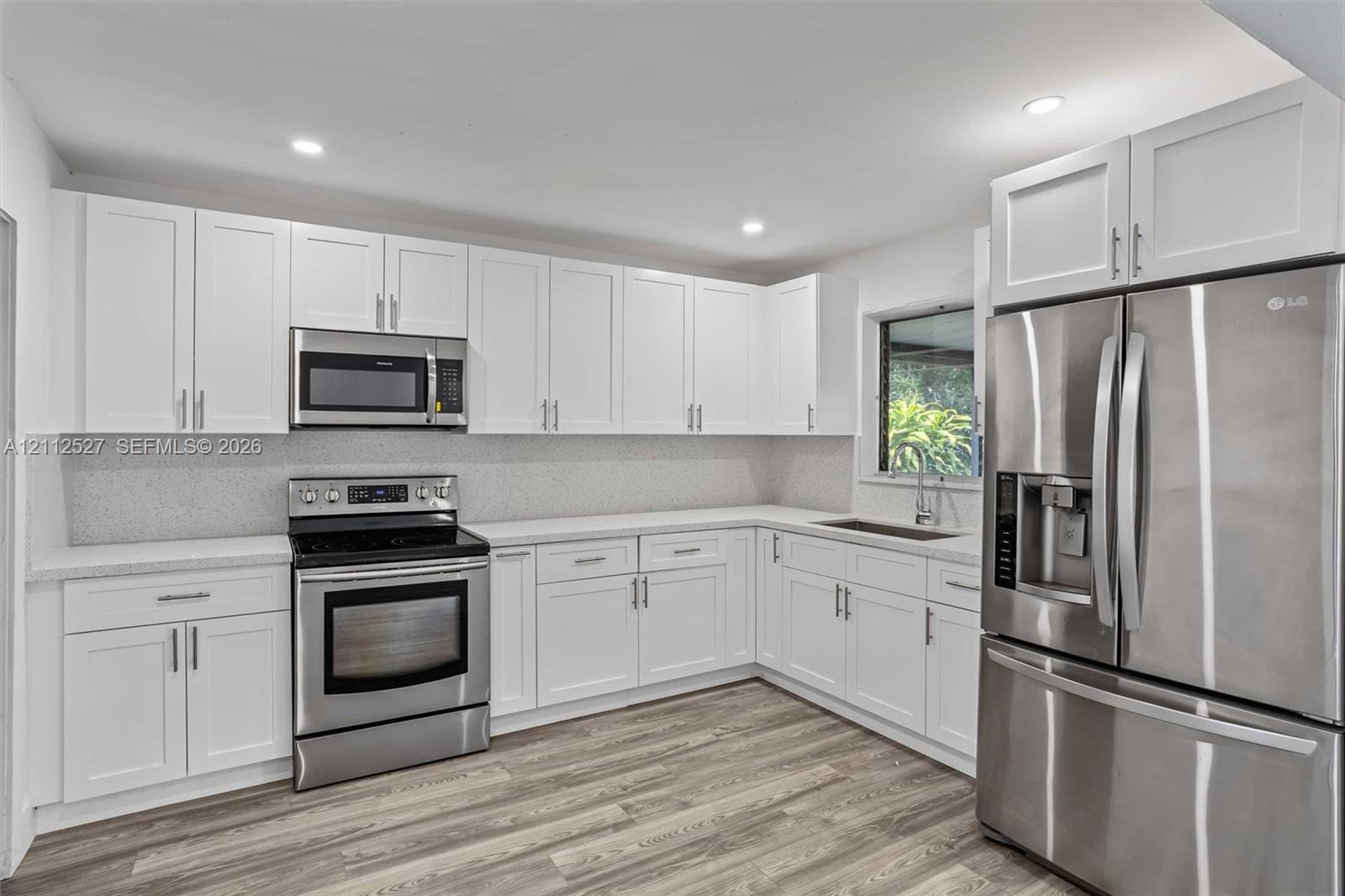 Kitchen featuring white Shaker-style cabinetry, stainless steel appliances, speckled stone-finish countertops, tile backsplash, and wood-finish flooring