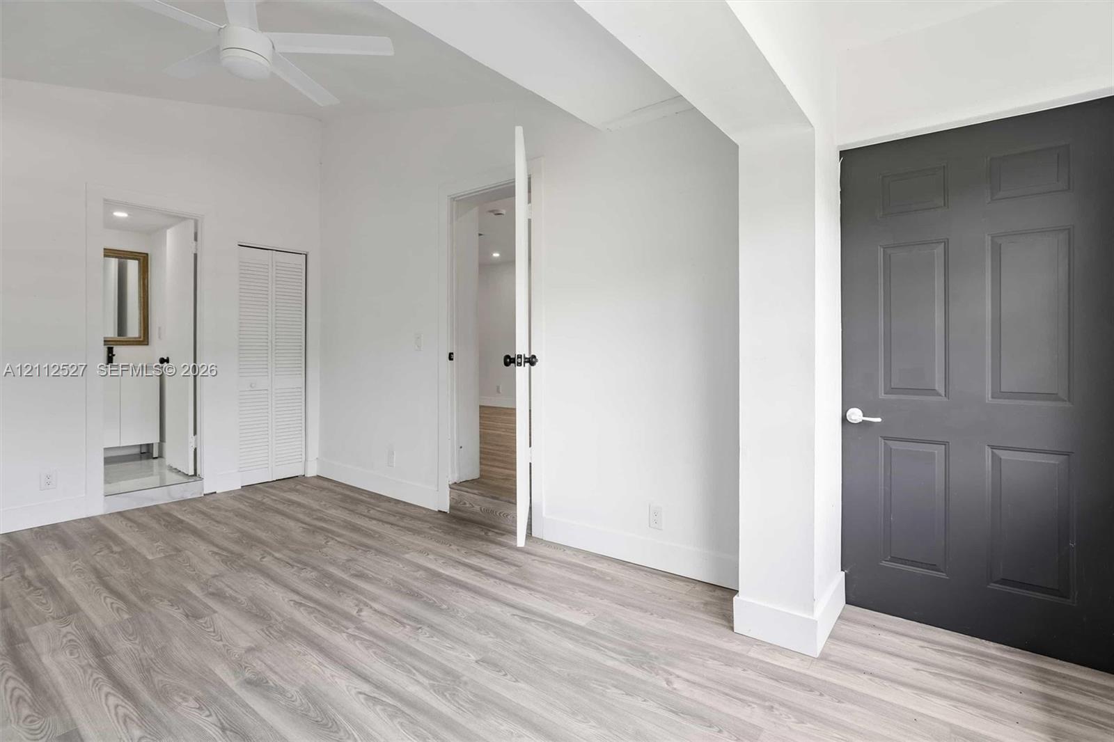 Interior space featuring wood-finish flooring, vaulted ceilings with a mounted ceiling fan, a charcoal-toned paneled door, and white louvered closet doors