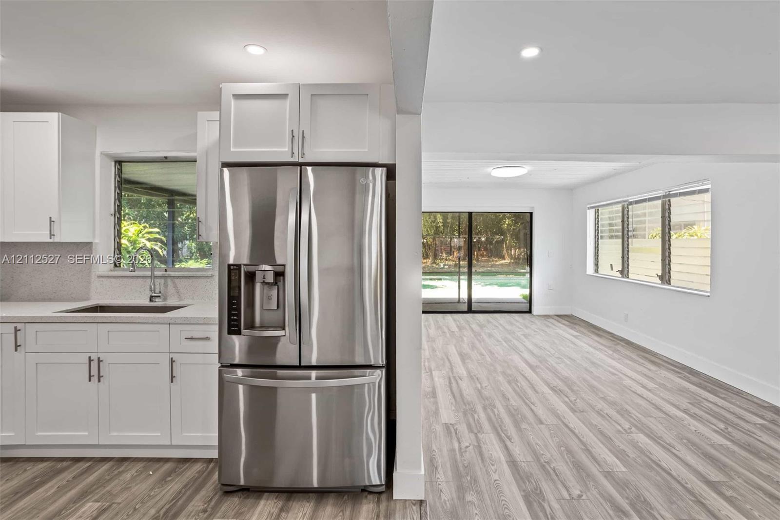 Kitchen featuring white shaker-style cabinetry, quartz countertops, stainless steel refrigerator, and wood-finish flooring with sliding glass doors
