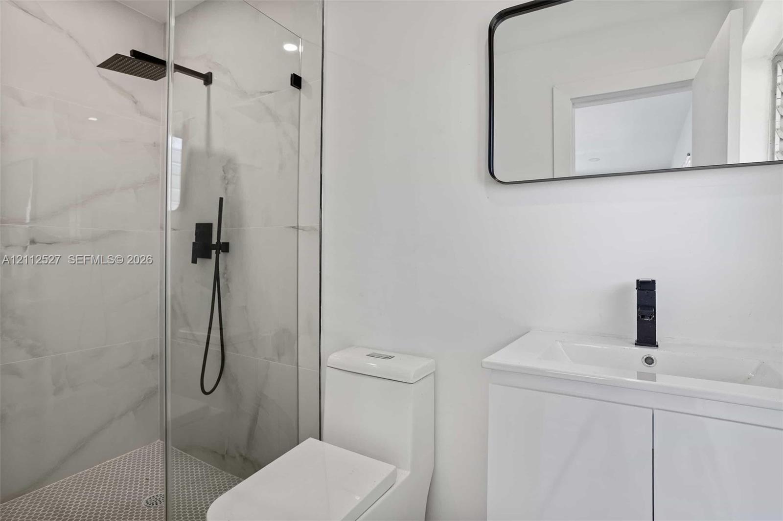 Walk-in shower featuring floor-to-ceiling stone-finish tile, matte black rainfall shower head, glass enclosure, white vanity with integrated sink, and matte black faucet