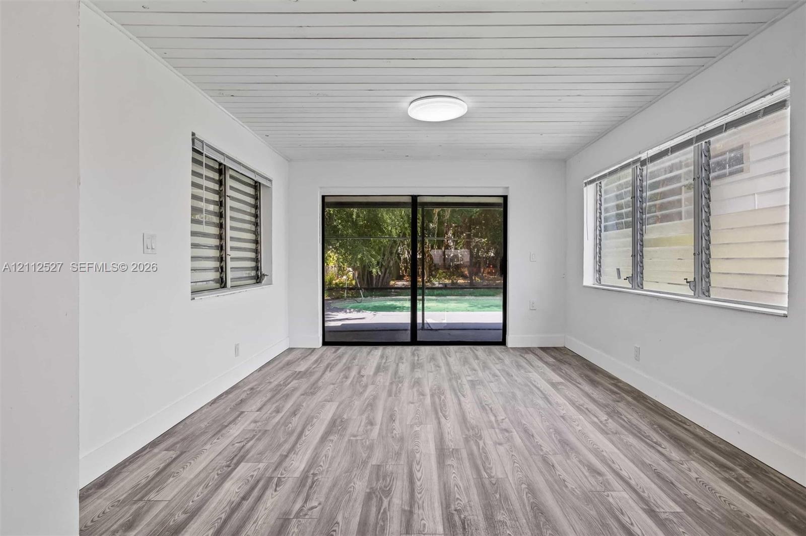 Wood-finish flooring, planked ceiling, sliding glass patio doors, and multi-pane windows with integrated blinds