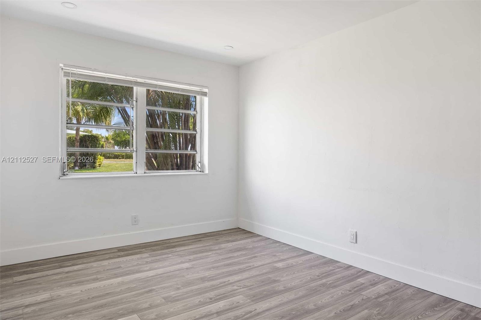 Room interior featuring wood-finish flooring, white walls, and a horizontal louvered window