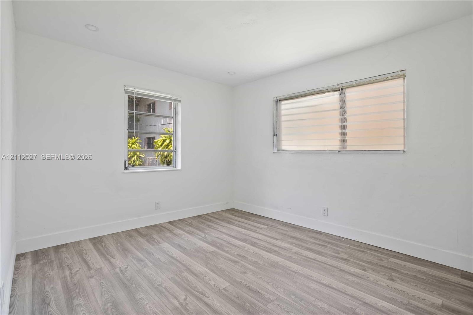Interior space featuring wood-finish flooring, white walls, recessed ceiling lighting, and windows equipped with fitted blinds