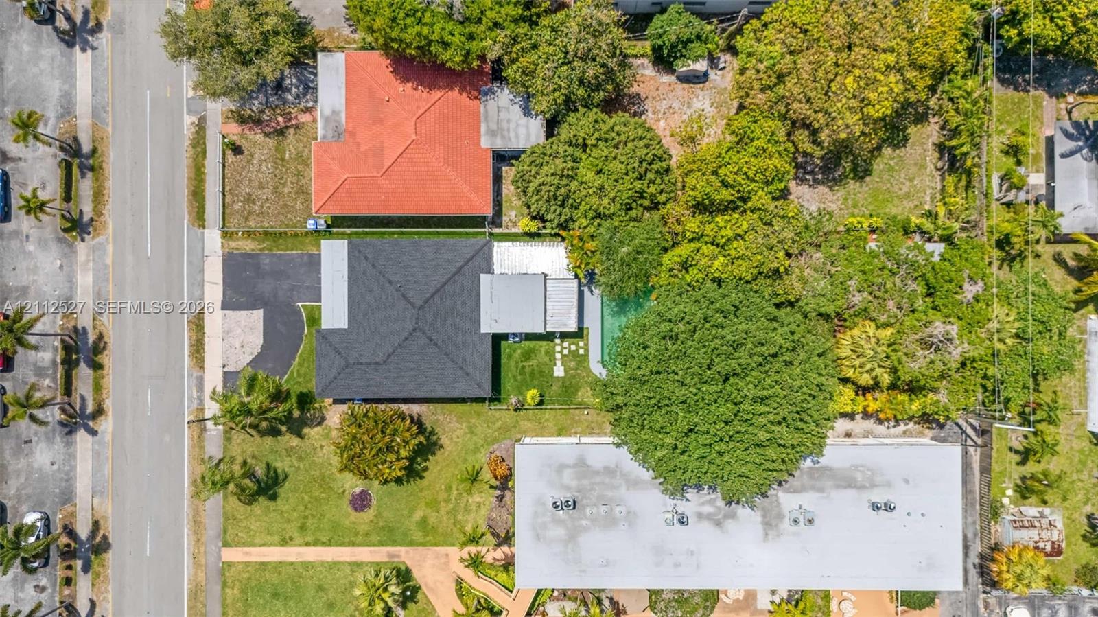 Aerial view of property featuring a dark-shingle roof, paved driveway, swimming pool, manicured lawn, and mature canopy trees