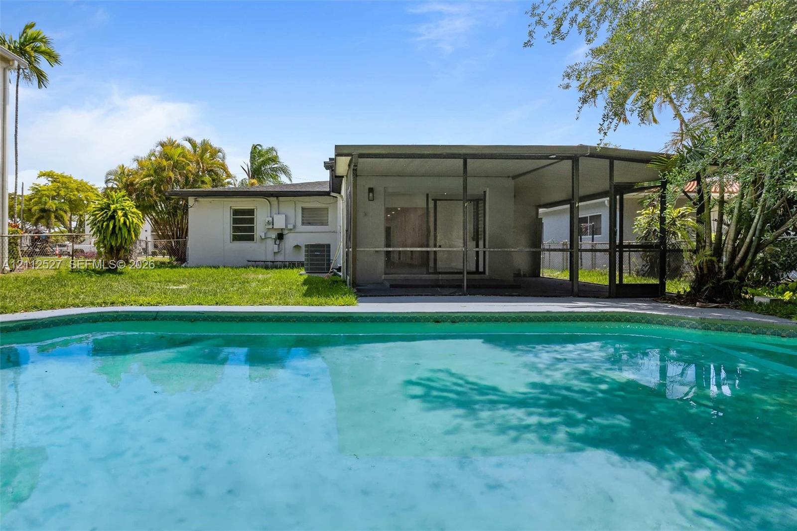 In-ground swimming pool featuring a concrete deck, screened-in lanai, and landscaped backyard