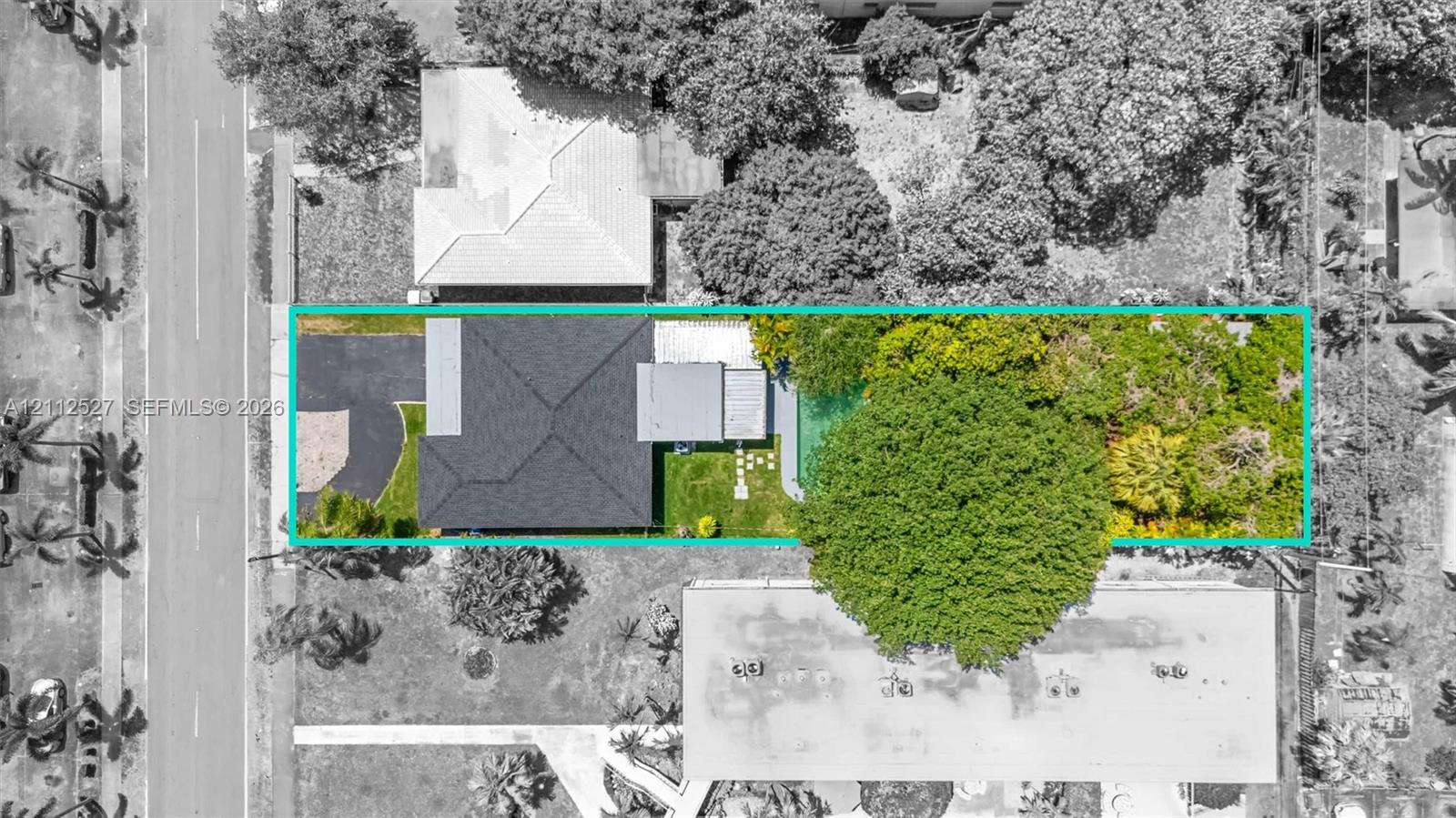 Aerial view of property featuring a dark-toned shingle roof, asphalt driveway, manicured lawn, stone-paver walkway, and mature landscaping