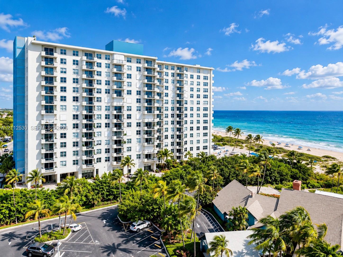 High-rise residential building featuring private balconies, expansive paved parking, and direct proximity to the oceanfront