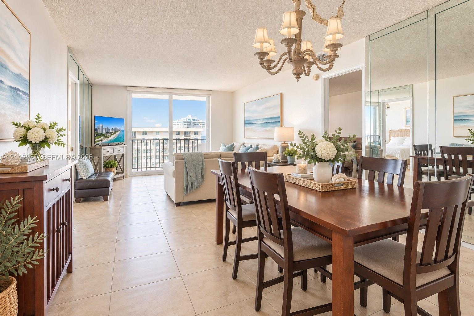 Open-concept living and dining area featuring large-format ceramic tile flooring, a multi-arm chandelier, full-height wall mirrors, and floor-to-ceiling sliding glass doors leading to a balcony