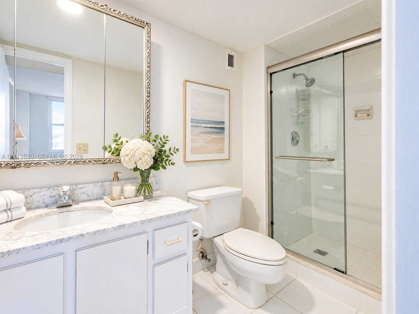 Bathroom featuring white cabinetry, stone-surface countertop, integrated vanity sink, large wall-mounted mirror, and a glass-enclosed shower with metallic hardware