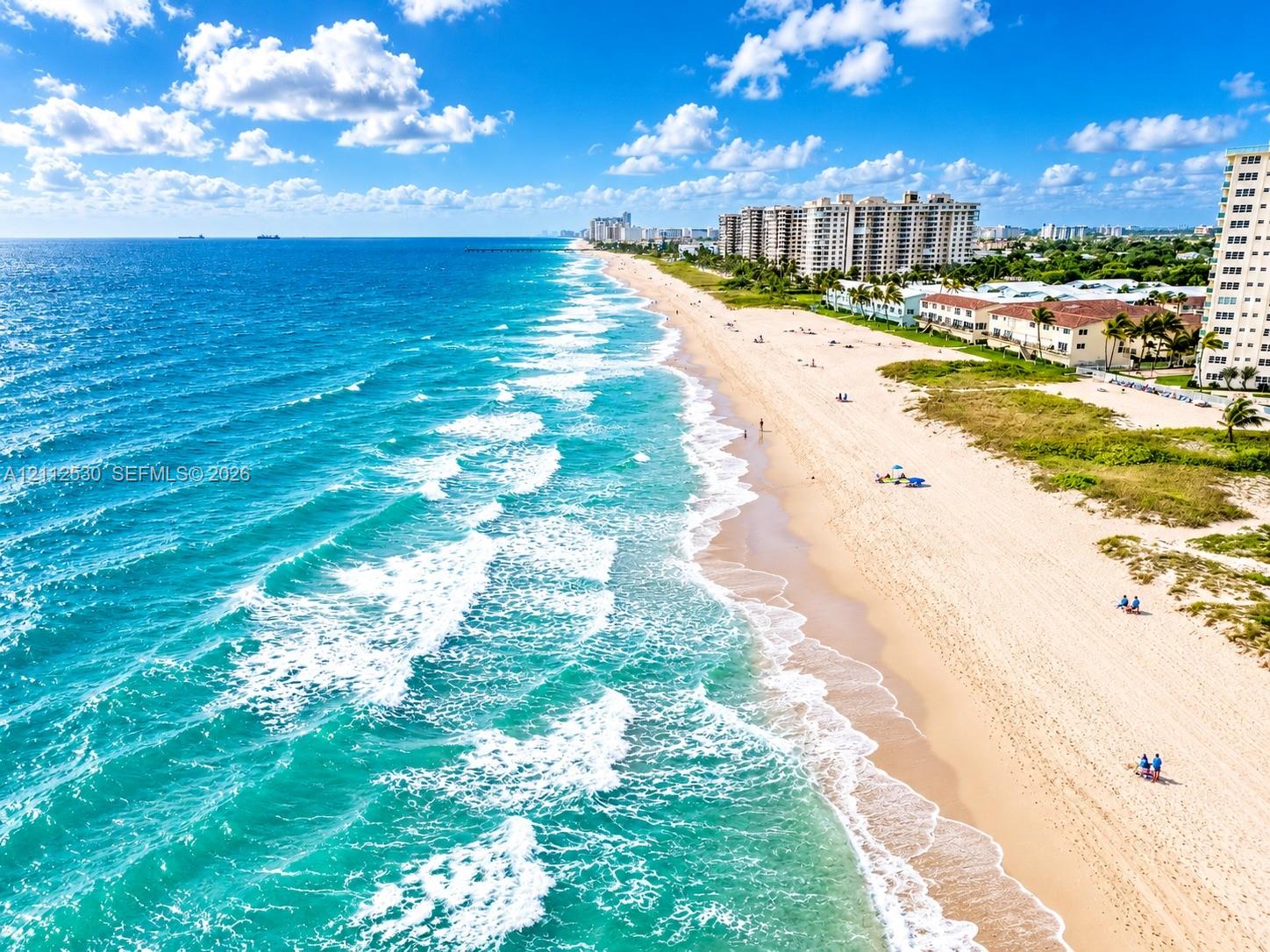 Aerial coastal landscape featuring direct oceanfront access, expansive sandy shoreline, and proximity to high-rise residential buildings