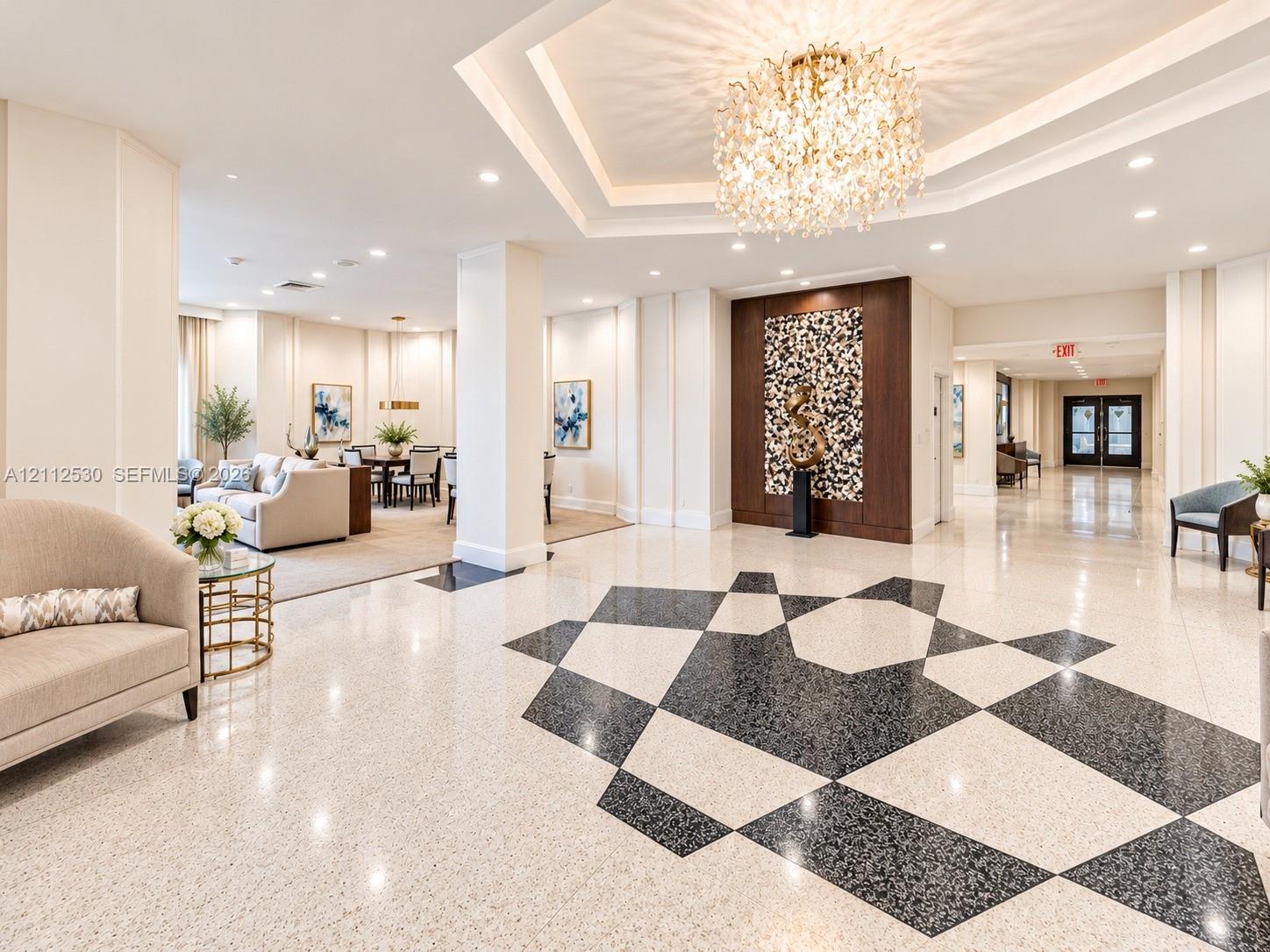 Grand lobby featuring geometric stone flooring, a multi-tiered tray ceiling, and a central crystal chandelier, accented by a dark wood-finish wall panel
