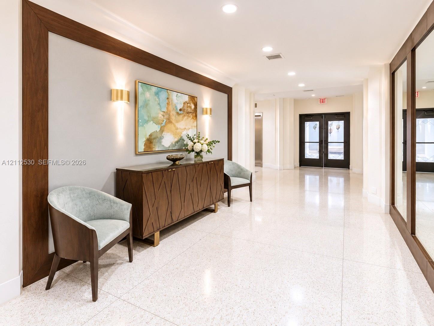 Polished stone flooring, wood-framed accent wall paneling, integrated wall-mounted lighting, and double-door entry