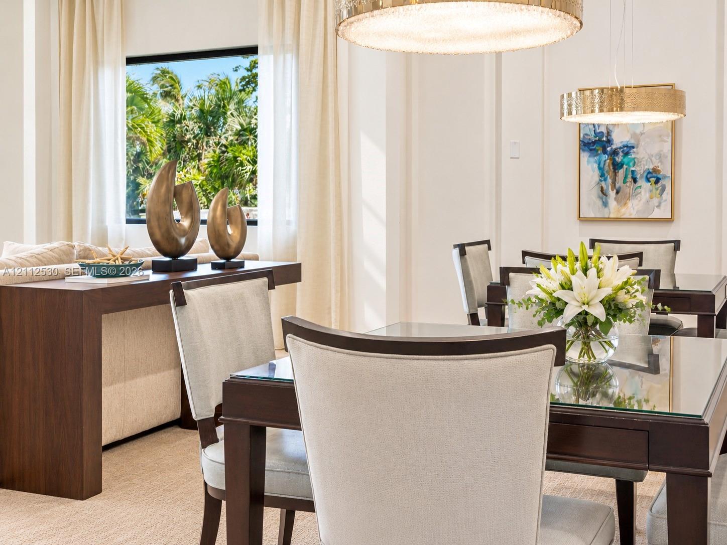 High ceilings featuring dual large drum-style chandeliers with metallic finishes, expansive picture window, and detailed wall molding