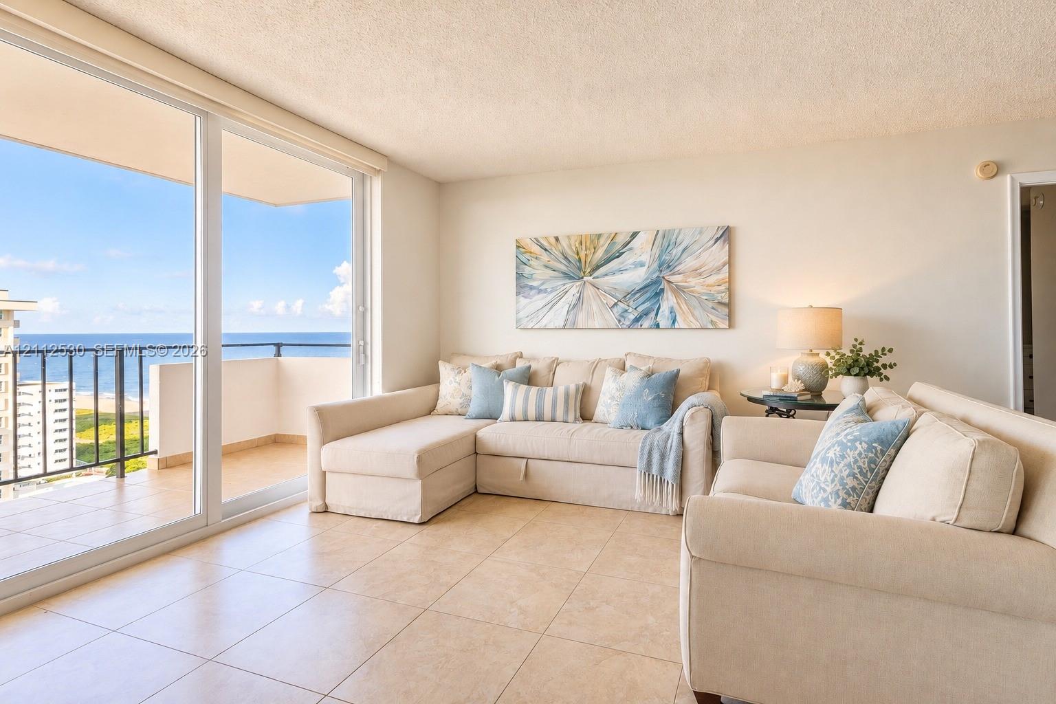 Open-concept interior featuring large-format ceramic tile flooring, floor-to-ceiling sliding glass doors, and a private balcony with ocean frontage
