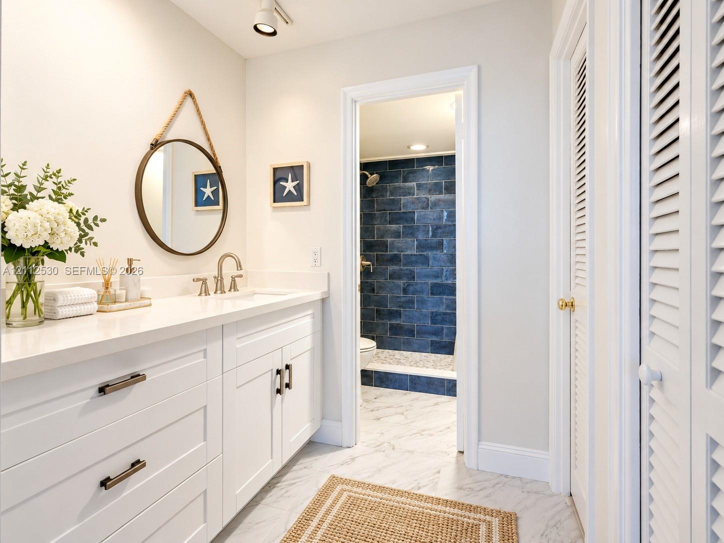 White cabinetry vanity with solid surface countertop, polished metal faucet, recessed ceiling lighting, and stone-finish flooring with a separate tiled shower enclosure