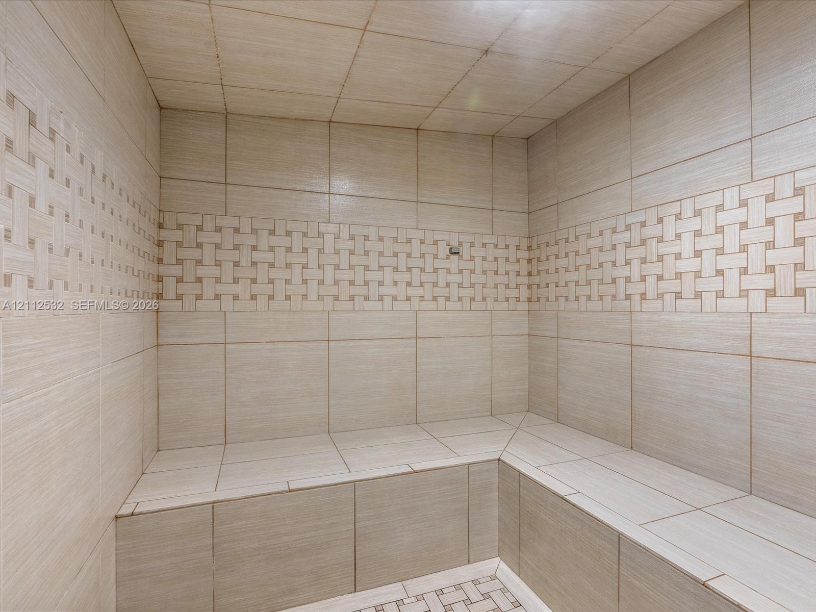 Tiled steam shower featuring built-in bench seating, large-format wall tiles, and decorative basket-weave accent detailing