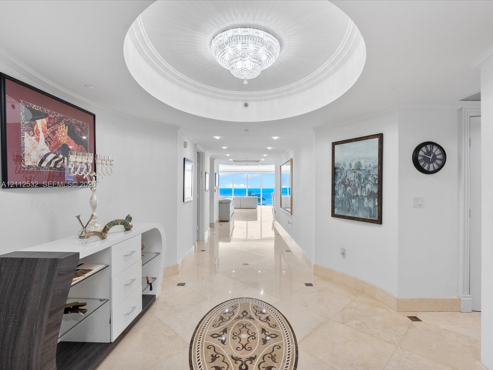 Foyer featuring a recessed circular tray ceiling, crystal chandelier, polished stone flooring with decorative inlay, and recessed lighting Foyer featuring a recessed circular tray ceiling, crystal chandelier, polished stone flooring with decorative inlay, and recessed lighting