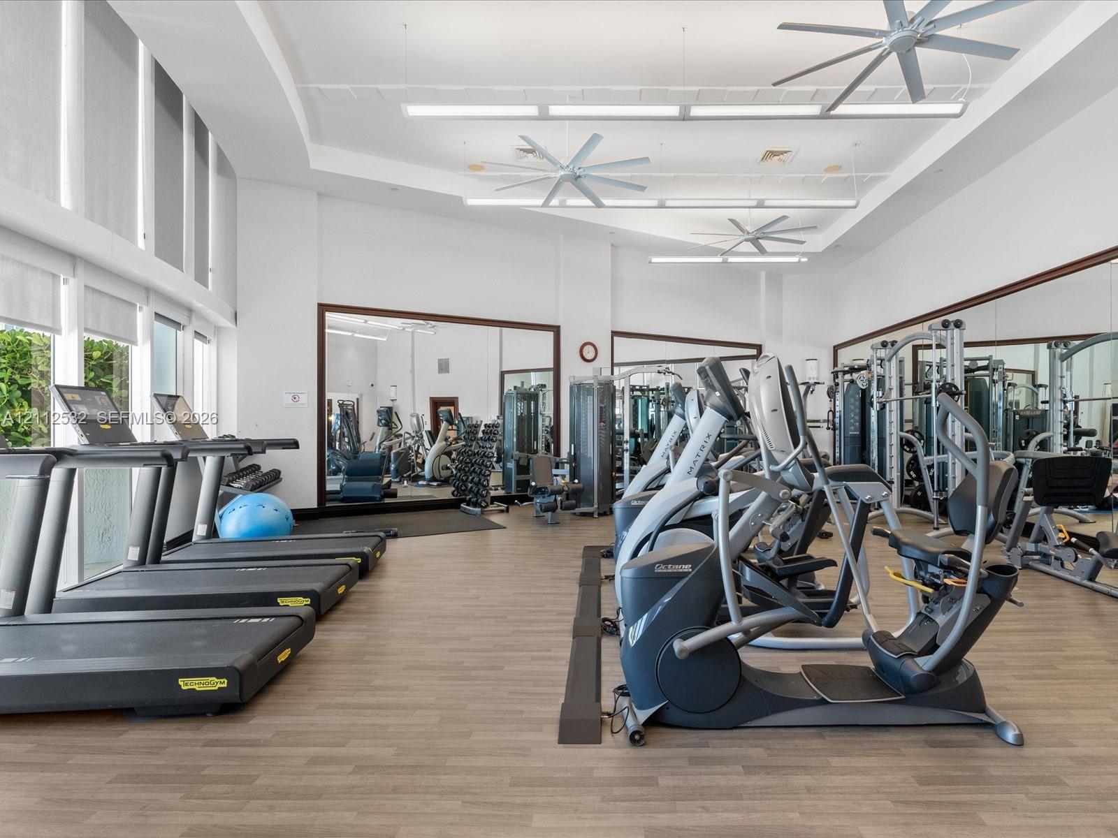 Fitness center featuring wood-finish flooring, floor-to-ceiling mirrored walls, recessed linear lighting, and ceiling-mounted fans