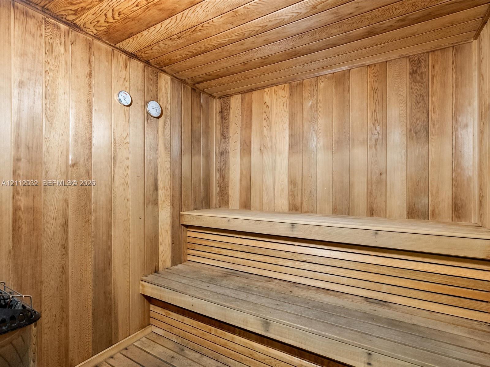 Sauna featuring natural wood-paneled walls and ceiling, tiered wood benches, and integrated wall-mounted analog gauges