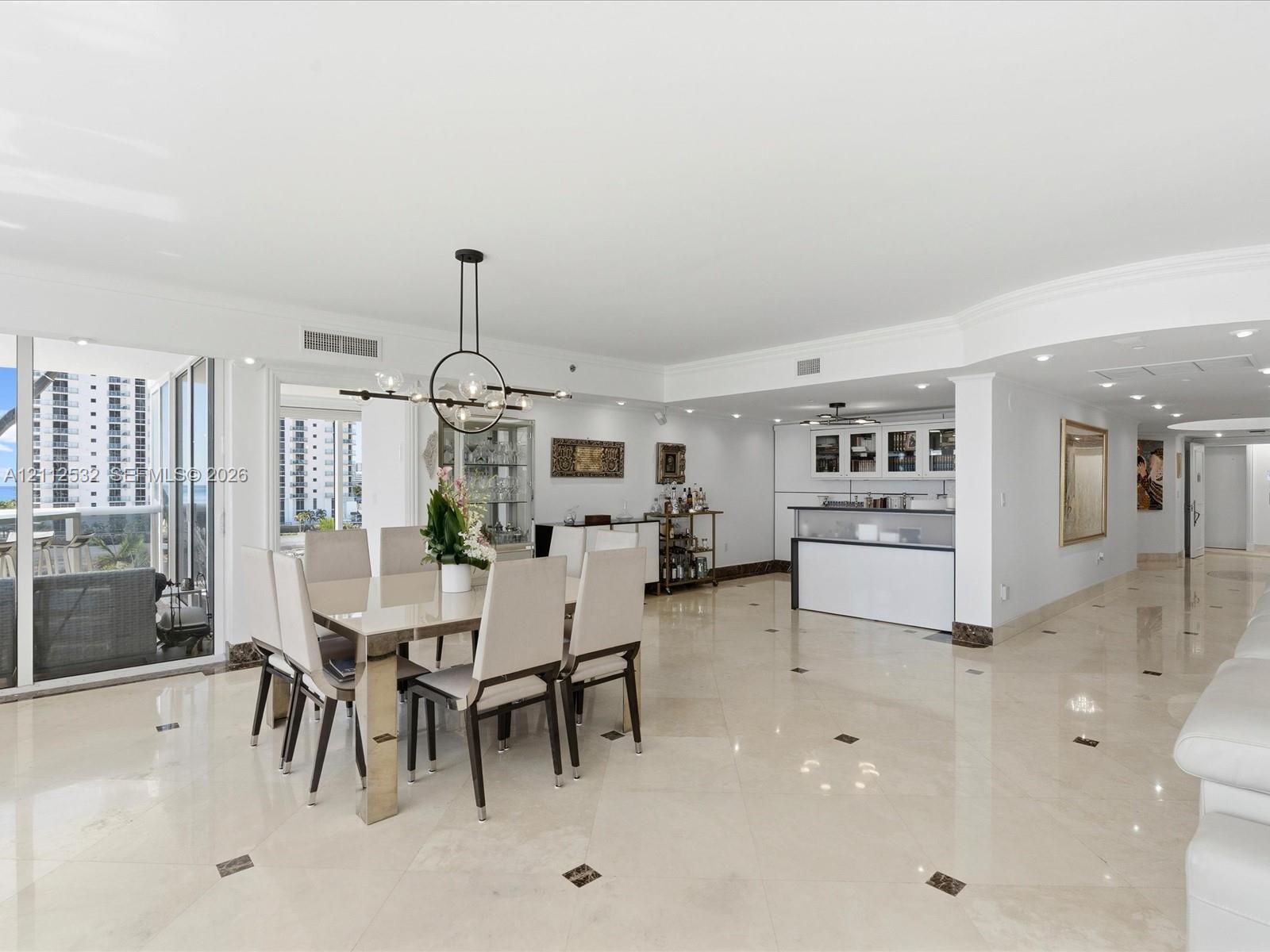 Open-concept area featuring polished stone flooring with decorative inlays, a built-in wet bar with cabinetry, recessed lighting, a modern multi-arm chandelier, and floor-to-ceiling glass sliding doors Open-concept area featuring polished stone flooring with decorative inlays, a built-in wet bar with cabinetry, recessed lighting, a modern multi-arm chandelier, and floor-to-ceiling glass sliding doors